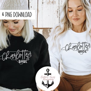 May include: Two women wearing black and white sweatshirts with the text "Charlotte Babe" and "Charlotte Bride" printed on them. The text is inside an outline of the state of North Carolina.