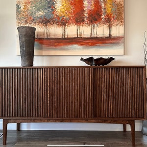 May include: A dark brown wooden cabinet with two sliding doors. The doors have vertical grooves and are closed. The cabinet is sitting on four legs and has a light brown top. There is a decorative bowl and a vase on the top of the cabinet.