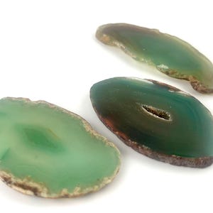 May include: Three green agate slices with brown edges. The agate slices are translucent and have a natural, organic shape.