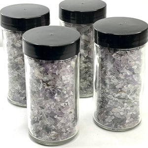 May include: Four glass jars filled with small, light purple amethyst crystals. The jars have black lids.