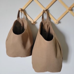 May include: Two brown canvas hanging storage baskets with a wooden hanging rack.