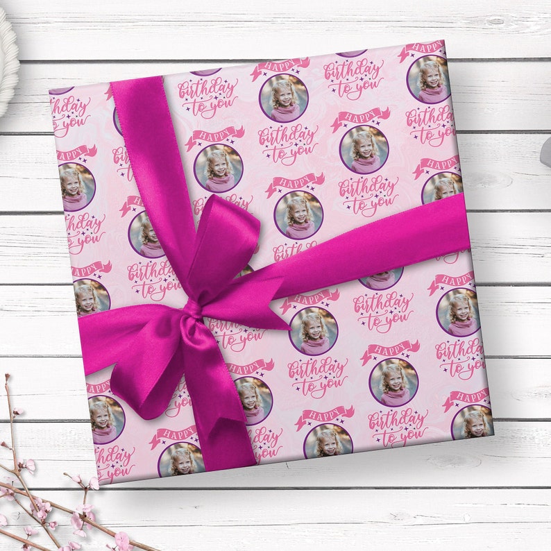 May include: Pink wrapping paper with a repeating pattern of white circles containing a photo of a child and the text "Happy Birthday to You".