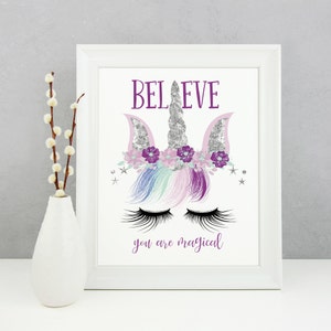 May include: A white framed print with a purple and silver glitter unicorn illustration. The unicorn has a silver horn, purple flowers, and closed eyes with long eyelashes. The text "BELIEVE you are magical" is printed below the unicorn.
