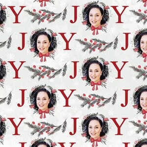 May include: A repeating pattern of the word "JOY" in red letters with a woman's face in a wreath of greenery and red berries. The background is a white and gray textured pattern.