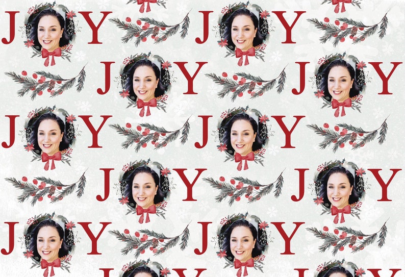May include: A repeating pattern of the word "JOY" in red letters with a woman's face in a wreath of greenery and red berries. The background is a white and gray textured pattern.