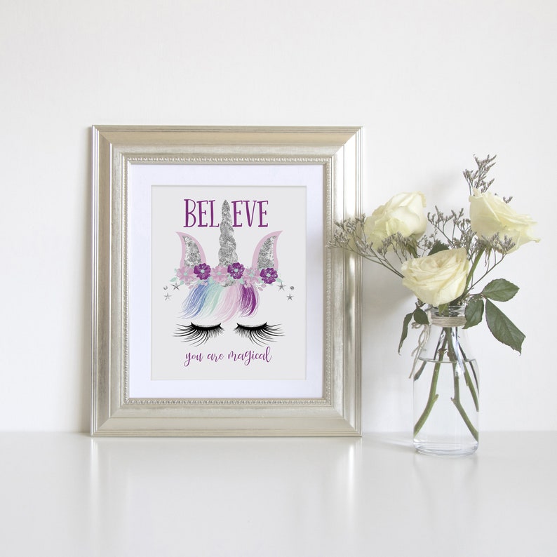 May include: A framed print with a unicorn illustration and the text "BELIEVE you are magical". The unicorn has a silver horn, purple flowers, and rainbow mane. The background is white.
