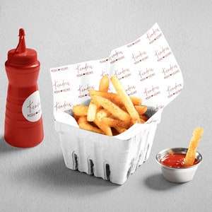 Pu&ograve; includere: Un cestino di carta bianco pieno di patatine fritte dorate. Il cestino &egrave; rivestito di carta bianca stampata con le parole "Kendra's Pizza & Vicente" in un font corsivo rosso. Una piccola bottiglia di ketchup di plastica rossa e una piccola ciotola di metallo con ketchup sono sul tavolo.