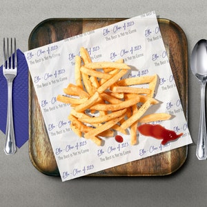 May include: A white paper bag with the text "Ella - Class of 2013 The Best is Yet to Come" printed on it. The bag contains a pile of french fries and a small amount of ketchup.