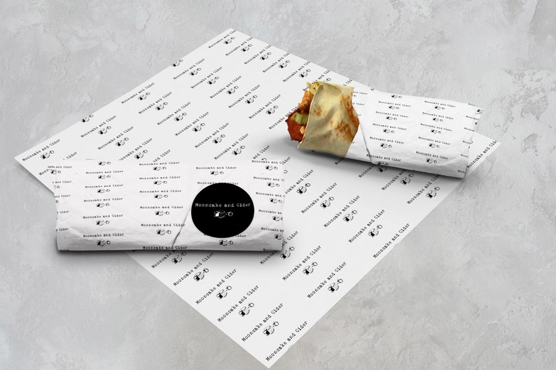Puede incluir: Papel de envolver blanco con un logotipo en blanco y negro que dice "Moonshake and Cider Co." Un burrito blanco y marr&oacute;n est&aacute; envuelto en el mismo papel.