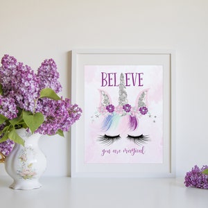 May include: A white framed print with a pink background and a unicorn illustration. The unicorn has a silver horn, purple flowers, and closed eyes. The text "BELIEVE you are magical" is printed below the unicorn.