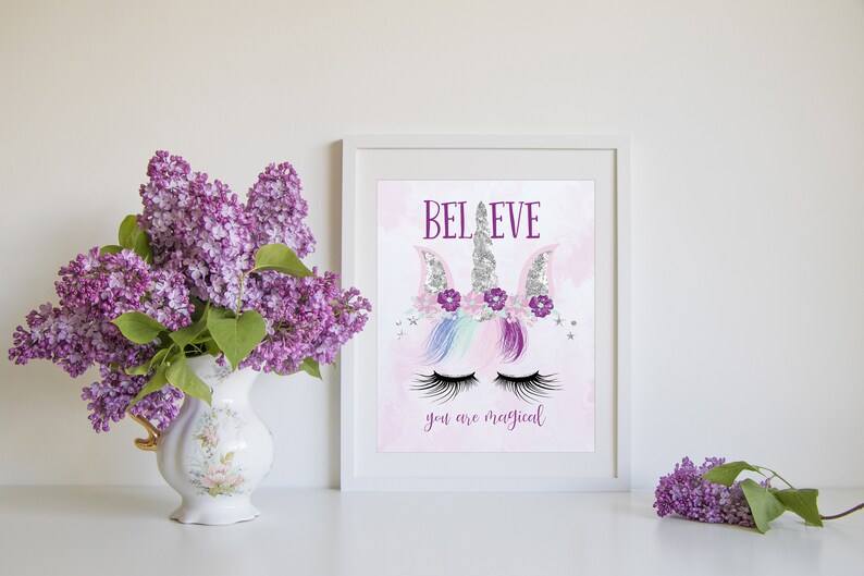 May include: A white framed print with a pink background and a unicorn illustration. The unicorn has a silver horn, purple flowers, and closed eyes. The text "BELIEVE you are magical" is printed below the unicorn.