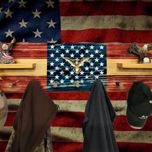 May include: A wooden coat rack with an American flag design. The rack has two shelves and five hooks. The flag is distressed and has a gold eagle in the center. There are two eagle figurines on the shelves.