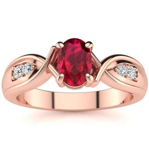 Peut inclure: Une bague en or rose avec une pierre précieuse ovale rouge rubis et deux diamants plus petits. La bague a un design de bande torsadée.