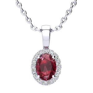 May include: A silver chain necklace with a pendant featuring a red oval gemstone surrounded by a halo of smaller white gemstones.