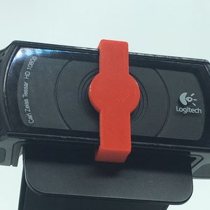 以下が含まれることがあります： 赤いクリップと側面に「Carl Zeiss Tessar HD 1080p」の文字が書かれた黒いロジクールウェブカメラ
