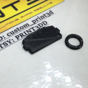 May include: A black 3D printed object with a rectangular shape and a textured surface. A smaller black 3D printed ring is also visible. The text "Pay ID: custom_print3d Etsy: PRINT3DD" is visible in the background.