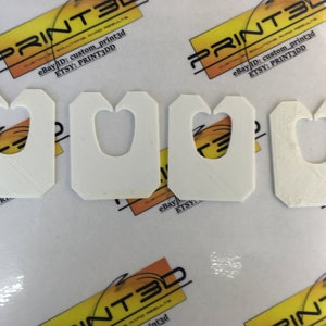 May include: Four white plastic pieces with a heart-shaped cutout. The pieces are designed to be used as a hanger for a product.