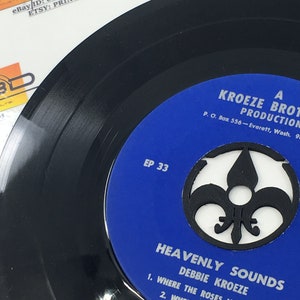 May include: A blue and black 45 RPM vinyl record with the title "Heavenly Sounds" by Debbie Kroeze. The record is labeled "EP 33" and features a fleur-de-lis design. The label also includes the text "A Kroeze Brothers Production, P.O. Box 556 - Everett, Wash. 9."