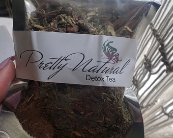 May include: A silver resealable pouch filled with loose leaf tea. The pouch has a white label with the text "Pretty Natural Detox Tea" and a butterfly graphic.