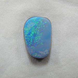 May include: A polished opal gemstone with a light blue base color and vibrant flashes of green and blue. The opal has an irregular, rounded shape and is set against a white background.