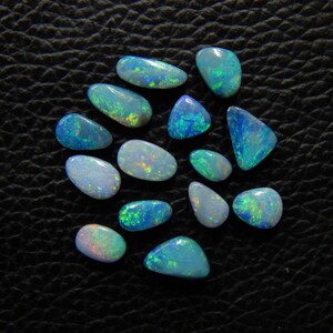 May include: A collection of polished opals in various shapes and sizes, showcasing a spectrum of colors including blues, greens, and flashes of other hues. The opals are set against a dark, textured background, highlighting their iridescent qualities.