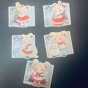 May include: Five Christmas-themed stickers featuring a cartoon girl with blonde hair and a red dress. The stickers have a sparkly, iridescent finish and depict the girl holding a Christmas tree, a snowman, and a gift.