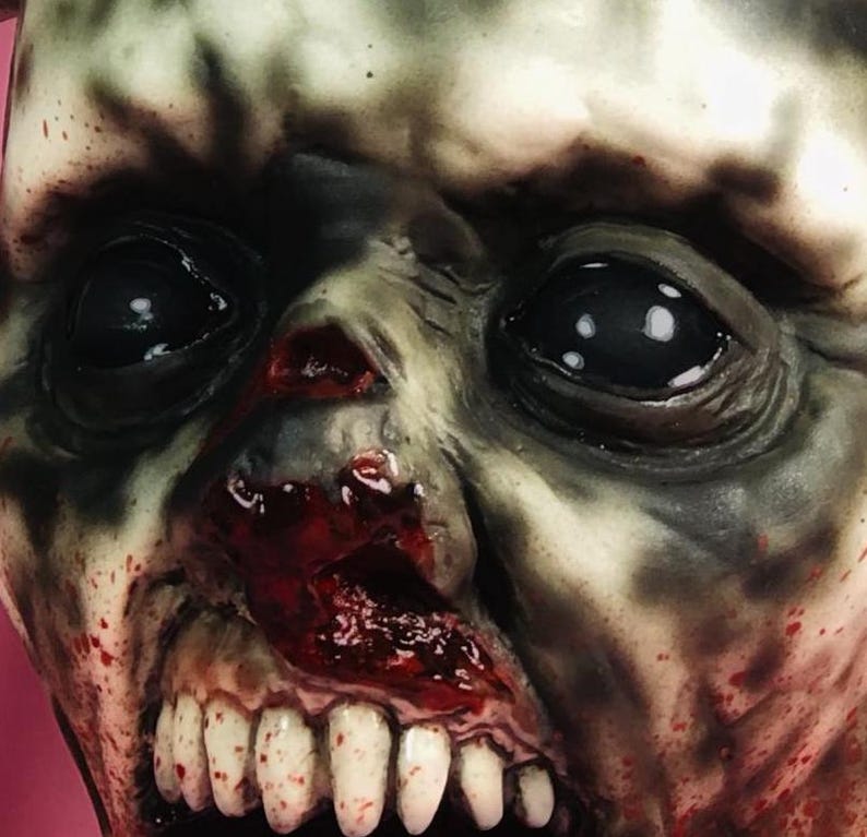 Może przedstawiać: Zbliżenie na realistyczną maskę zombie z krwawą, otwartą paszczą i odsłoniętymi zębami. Maska ma szarą i zieloną karnację z realistycznymi szczeg&oacute;łami, w tym zmarszczkami i rozpryskami krwi.