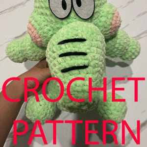May include: A light green crochet monster with large gray eyes, pink cheeks, and black stripes. The text "CROCHET PATTERN" is overlaid in red. The plush toy has small arms and legs, and gray and white striped horns.