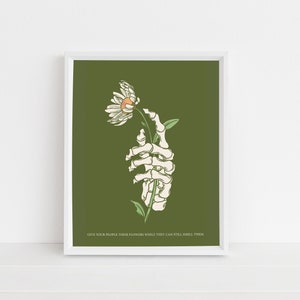 May include: A skeletal hand holding a white daisy with a yellow center against a dark green background. The text "Give your people their flowers while they can still smell them" is at the bottom of the image.