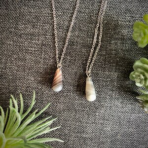 Peut inclure: Deux colliers en argent avec des pendentifs en agate en forme de larme. Un pendentif est gris et blanc, l'autre est brun et blanc.
