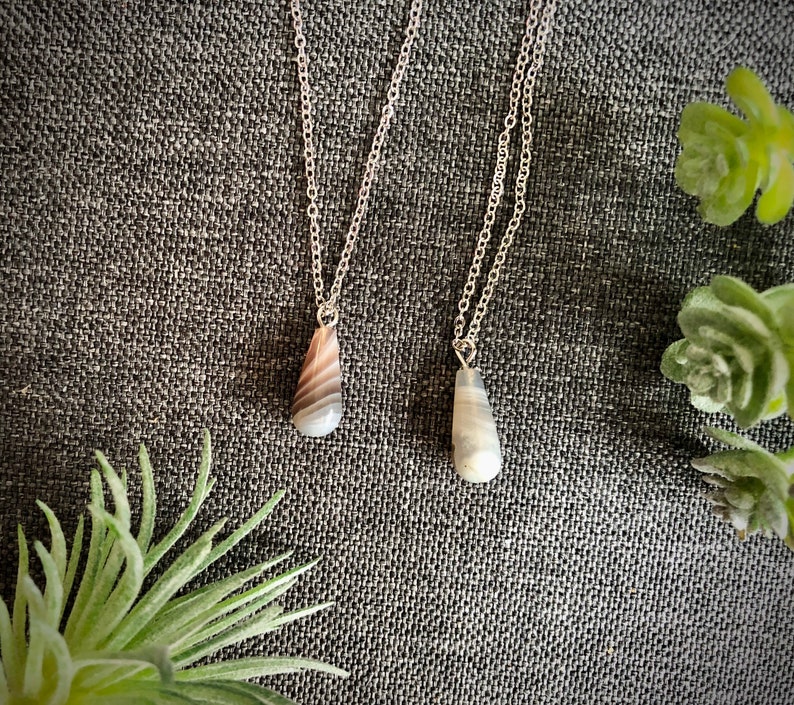 Peut inclure: Deux colliers en argent avec des pendentifs en agate en forme de larme. Un pendentif est gris et blanc, l'autre est brun et blanc.