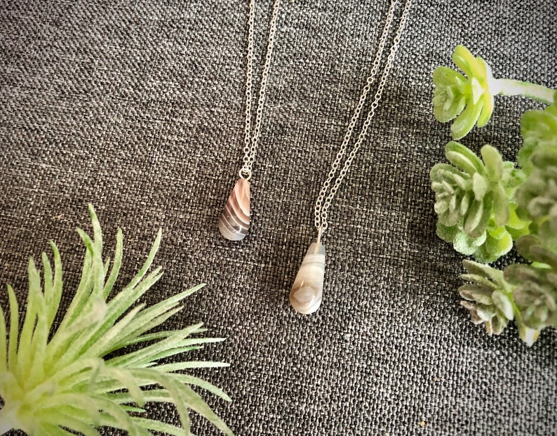 Peut inclure: Deux colliers en argent avec des pendentifs en forme de larme en agate. L'agate est de couleur brun clair et blanc avec un motif tourbillonnant.