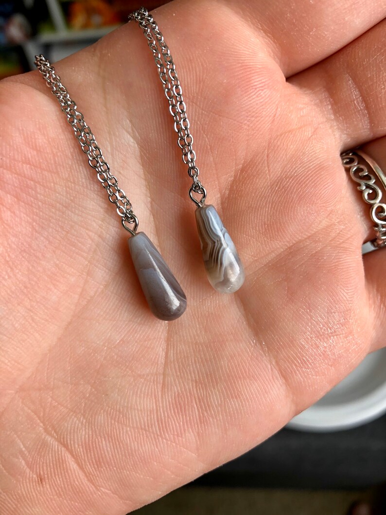 Peut inclure: Deux cha&icirc;nes en argent avec des pendentifs en agate grise. Les pierres sont en forme de larme et pr&eacute;sentent un motif marbr&eacute; blanc et gris.