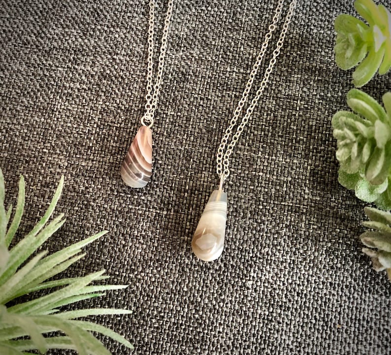 Peut inclure: Deux colliers en argent avec des pendentifs en agate en forme de larme. Les pendentifs sont de couleur brun clair avec des tourbillons blancs et gris.