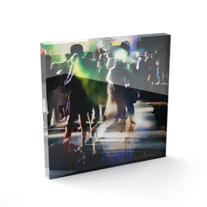 Può includere: Un gruppo di persone che ballano in una stanza scarsamente illuminata con luci verdi e blu. Le persone sono in silhouette contro le luci e i loro volti non sono visibili.