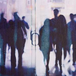 Peut inclure: Une image floue de personnes marchant à travers une porte en verre. Les personnes sont en silhouette sur un fond lumineux, et leurs traits ne sont pas visibles. L'image est dans des tons de bleu et de violet.