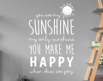 Peut inclure: Autocollant mural en vinyle blanc avec le texte "You are my sunshine, my only sunshine, you make me happy, when skies are grey". Un graphique de soleil souriant est au-dessus du texte.