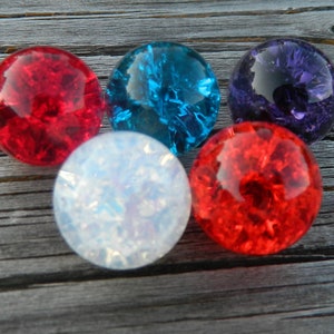 May include: Five glass marbles in various colors, including red, blue, purple, and white. The marbles have a textured, iridescent surface.