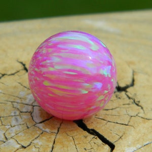 May include: A pink opal bead with iridescent white and green streaks. The bead is round and smooth.