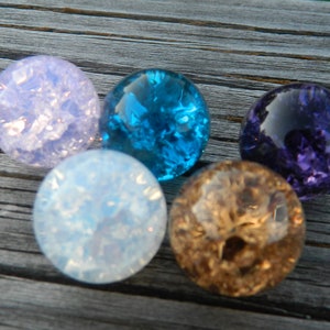 May include: Five glass marbles in various colors, including purple, blue, light blue, and white. The marbles have a textured, iridescent surface.
