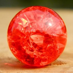 Può includere: Una biglia di vetro rosso brillante con un motivo a spirale e nuvoloso all'interno.