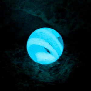 以下が含まれることがあります： 渦巻き模様の光る青と白の大理石。大理石は暗い場所で照らされています。