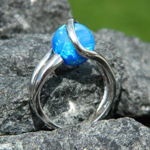 May include: A silver ring with a blue opal gemstone. The ring has a twisted band design.