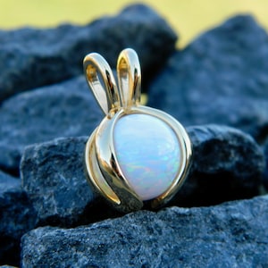 May include: A gold pendant with a round white opal gemstone. The pendant has a delicate, ornate design.
