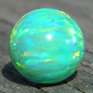 May include: A round green opal gemstone with iridescent blue and yellow flashes.