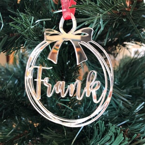 May include: Silver mirrored Christmas ornament with a red ribbon and the name "Frank" inscribed on it.