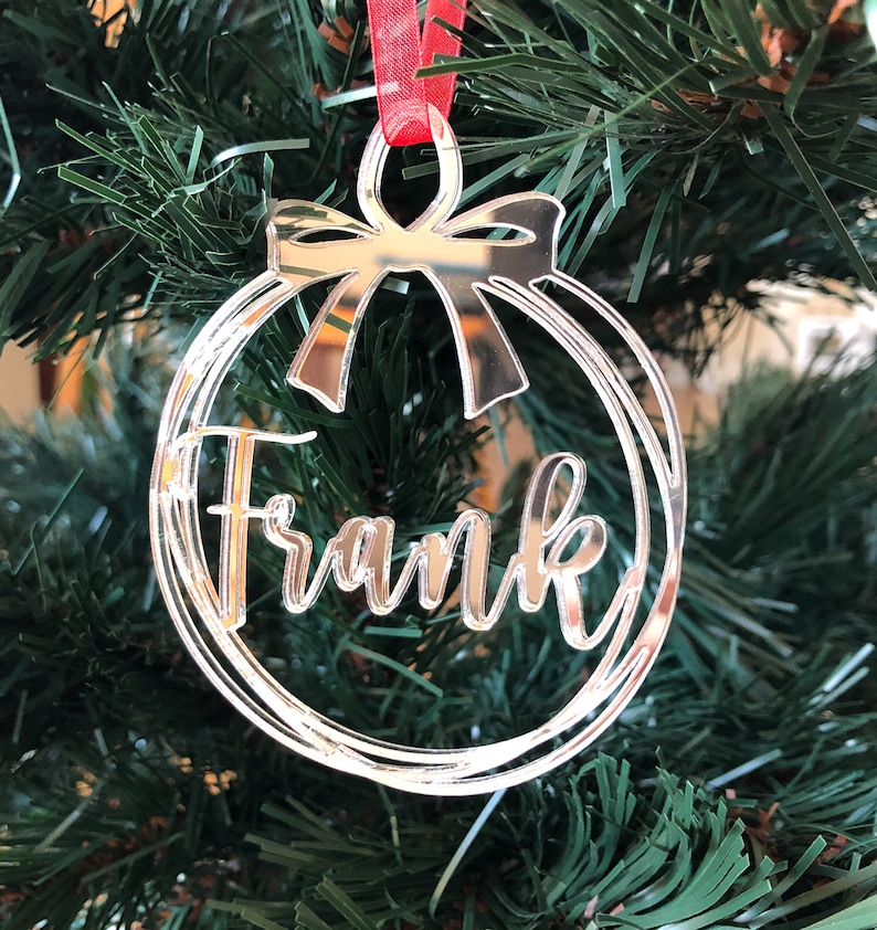 May include: Silver mirrored Christmas ornament with a red ribbon and the name "Frank" inscribed on it.