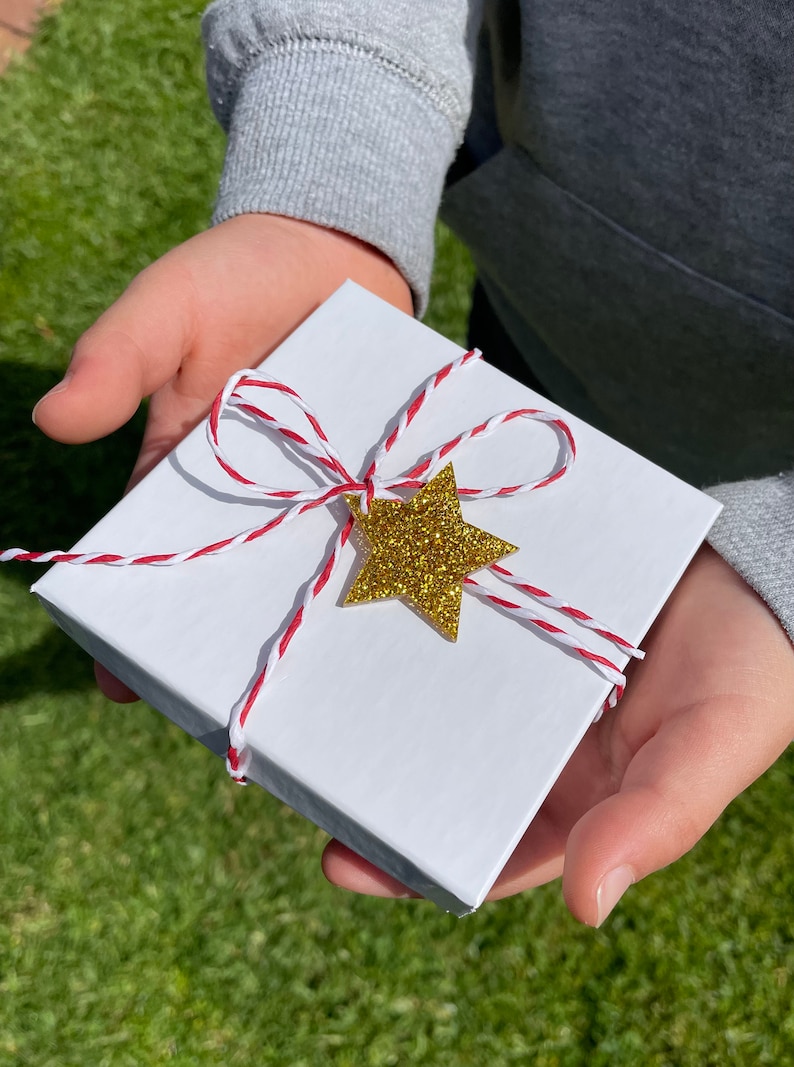 May include: A white gift box tied with red and white baker's twine and a gold glitter star.