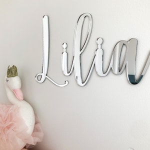 May include: Silver mirror acrylic name sign with the name "Lilia" in a cursive font.