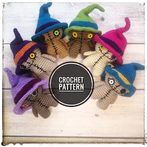 May include: Six crocheted voodoo dolls with different colored hats. The hats are purple, orange, green, pink, blue, and blue with yellow trim. The dolls are all brown and have black button eyes. The dolls are arranged in a circle on a white wooden surface. CROCHET PATTERN is written in black on a white circle in the center of the image.